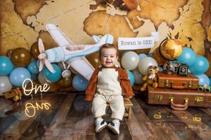 Baby boy Rowan celebrates his first birthday with a travel-themed photo shoot featuring a toy plane, balloons, and vintage suitcases.