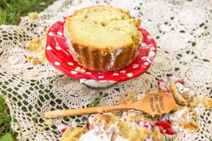 Golden bundt cake on red polka dot plate with wooden spoon on lace cloth outdoors.