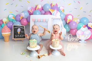 Twin babies celebrate first birthday with ice cream theme, colorful balloons, and individual smash cakes in a festive photo shoot.