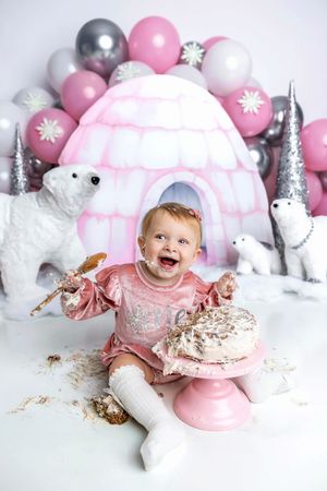 Laughing baby girl celebrating first birthday cake smash with polar bear and igloo decorations.