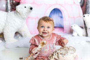 Baby girl in pink outfit smashing her first birthday cake surrounded by polar bear decorations.