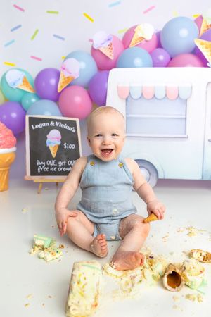 Baby smiling during ice cream themed first birthday cake smash with colorful balloons and decorations.