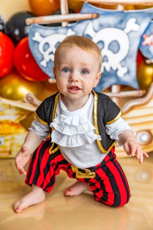 Adorable baby dressed in a pirate costume with red striped pants at a pirate-themed birthday party.