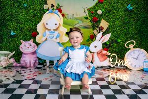 Baby girl in Alice in Wonderland themed first birthday cake smash with Cheshire Cat and White Rabbit decorations.