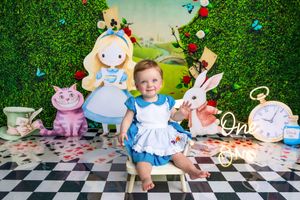 Baby girl in Alice in Wonderland themed first birthday photo shoot with Cheshire Cat and White Rabbit cutouts.