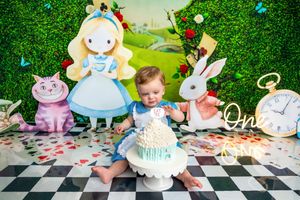 Baby's first birthday cake smash in Alice in Wonderland theme with chess floor backdrop and character cutouts.