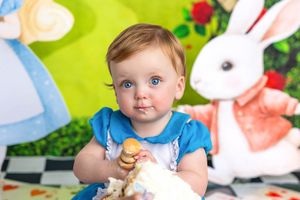 Baby in blue dress with blue eyes eating cake at Alice in Wonderland themed first birthday party.