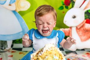 Crying baby in Alice in Wonderland costume during messy first birthday cake smash photography session.