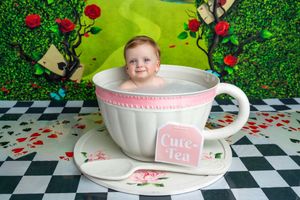 Adorable baby sitting inside a giant decorative teacup prop with Alice in Wonderland themed backdrop.