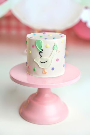 Small white cake with colorful polka dots and a duck decoration on a pink cake stand.