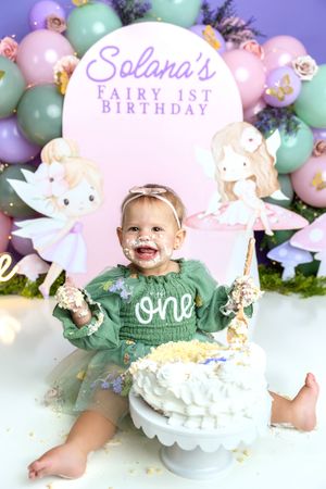 Baby girl celebrates Solana's Fairy 1st Birthday smashing a white cake, wearing a green tutu dress.