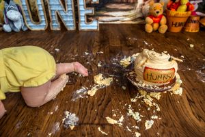 Baby smashing a Winnie the Pooh Hunny pot cake on a wooden floor at a first birthday cake smash.