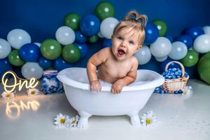 Baby's first birthday cake smash in white tub with blue green balloons and One neon sign.