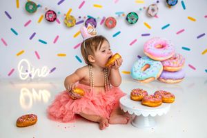 Baby girl in pink tutu eats donuts at colorful first birthday cake smash photo session with donut theme.