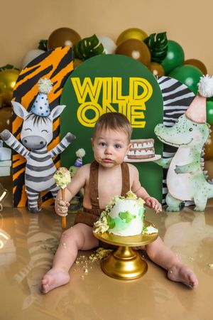 Baby smashes first birthday cake at a Wild One safari-themed party with zebra and crocodile decorations.