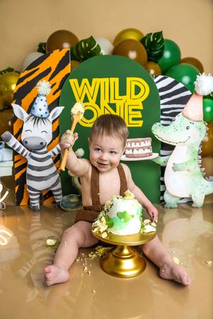 Baby's first birthday cake smash with Wild One safari theme, green balloons, zebra and crocodile decorations.