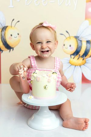Baby girl smiling during a bee-themed first birthday cake smash with a decorated white cake.
