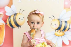 Baby girl in pink romper eating cake at a bee-themed first birthday smash cake photoshoot.