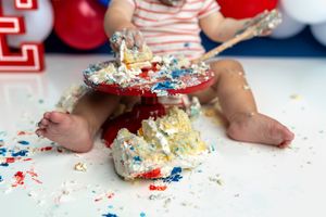 Baby smashing first birthday cake with red, white, and blue frosting during a cake smash celebration.
