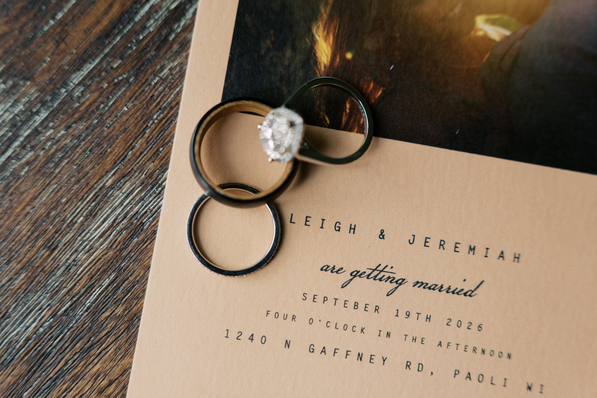 Wedding rings and diamond engagement ring resting on kraft paper wedding invitation for Leigh and Jeremiah.