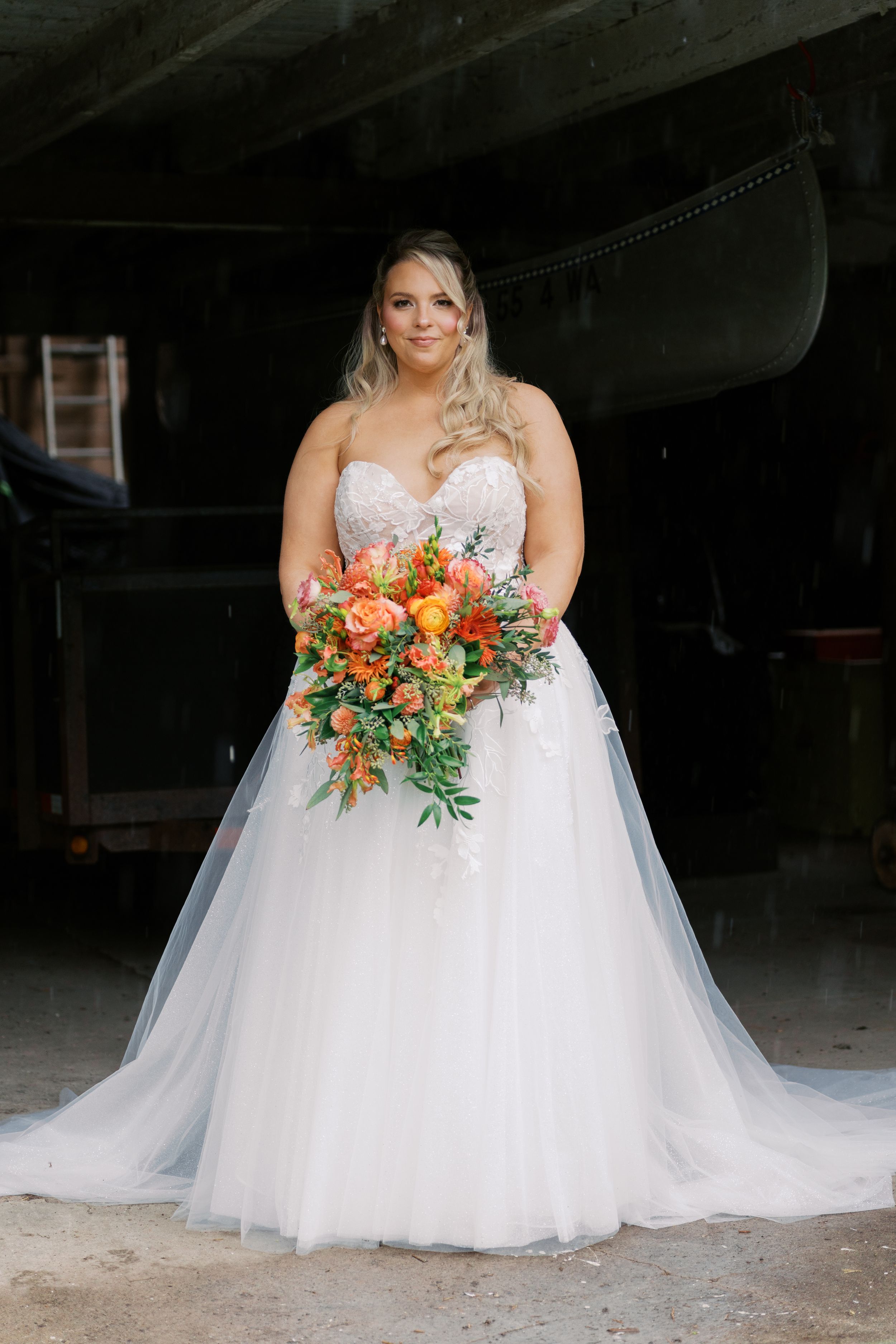 Bride in a white tulle ball gown holding a vibrant orange and pink floral bouquet, posing elegantly indoors.