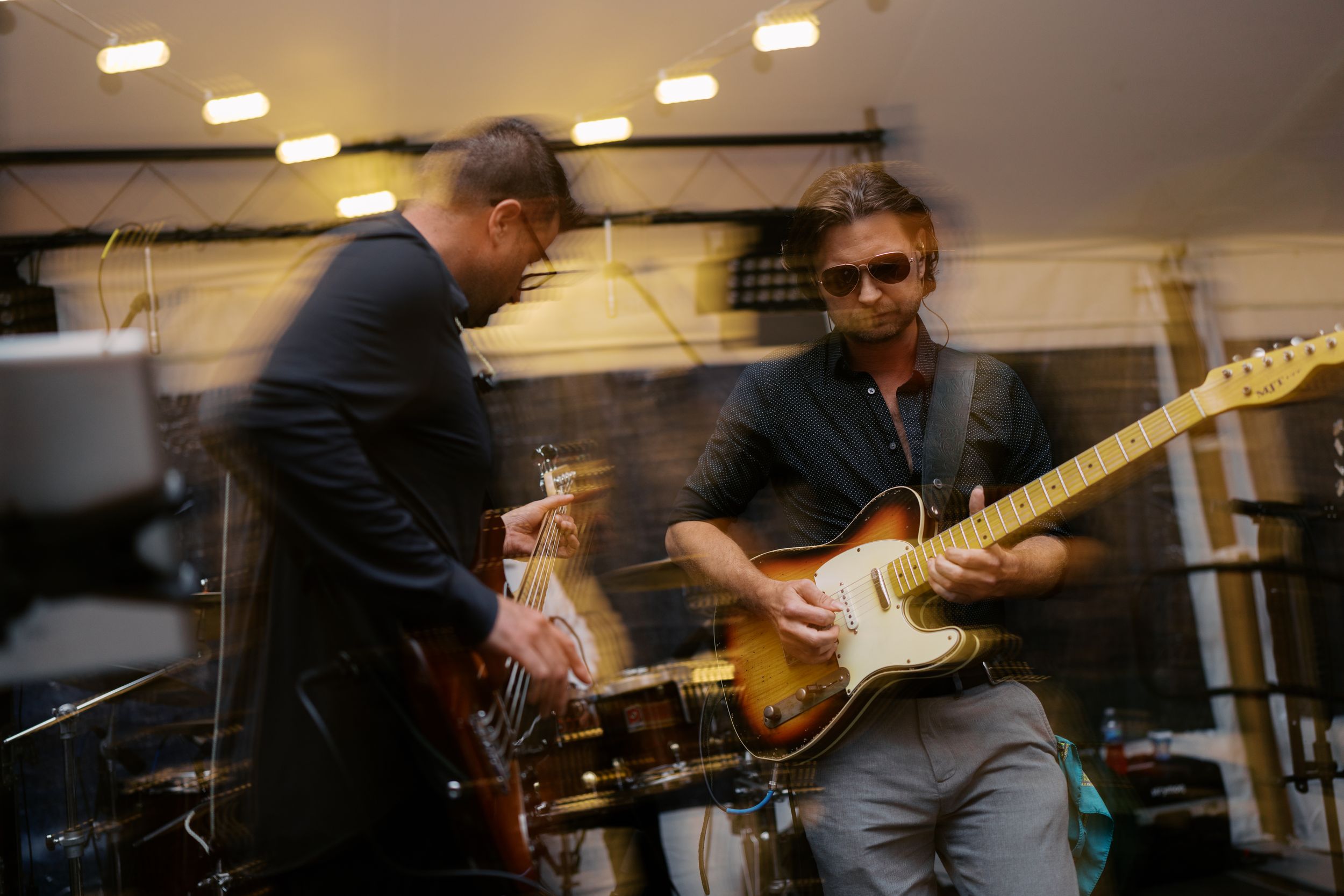 Two male musicians performing live, one playing electric guitar on stage with motion blur and dramatic lighting.