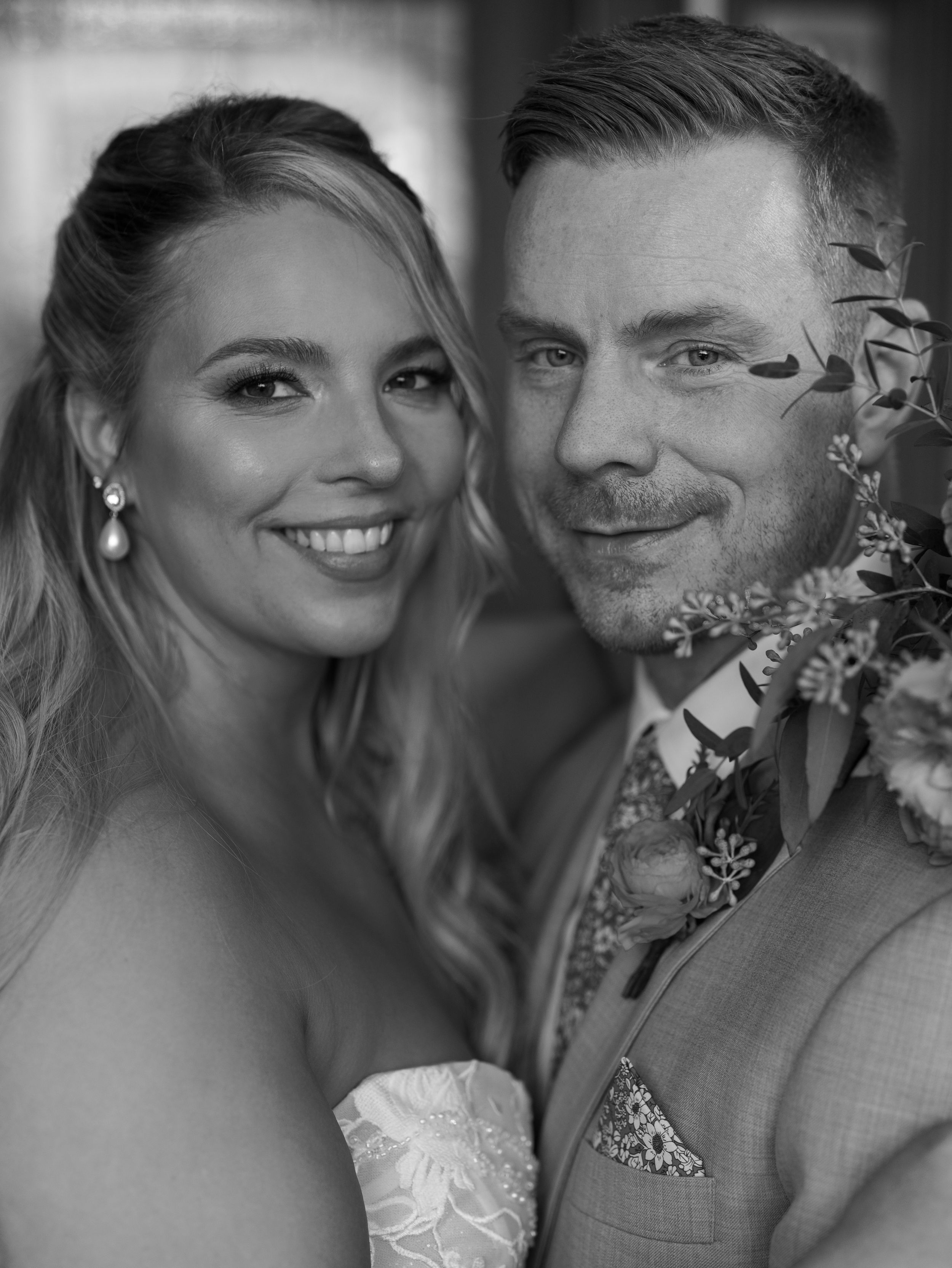 Black and white wedding portrait of a smiling bride and groom posing together with floral decorations.