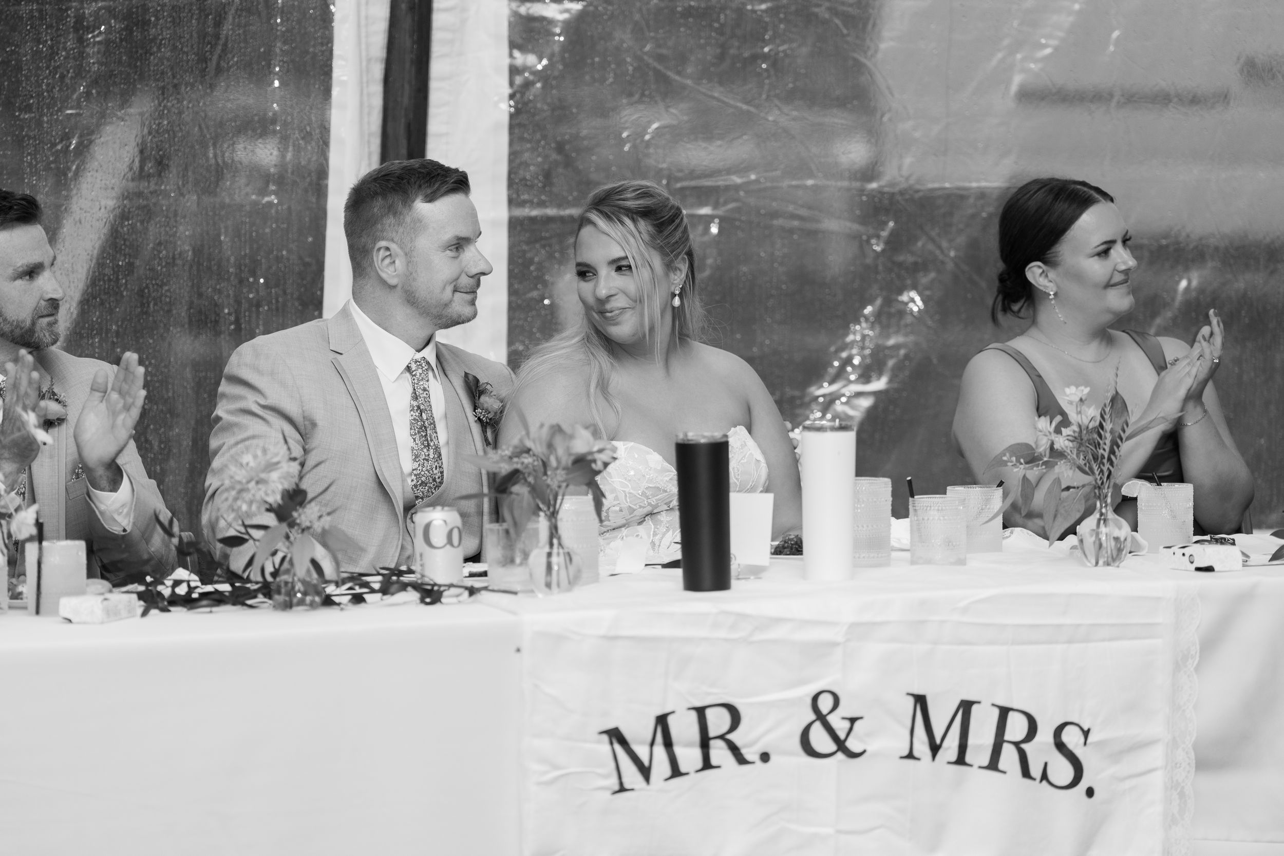 Black and white wedding reception photo of bride and groom seated at head table with Mr. & Mrs. sign.