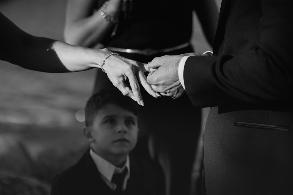 Black and white wedding ring exchange photo with child watching ceremony in background.