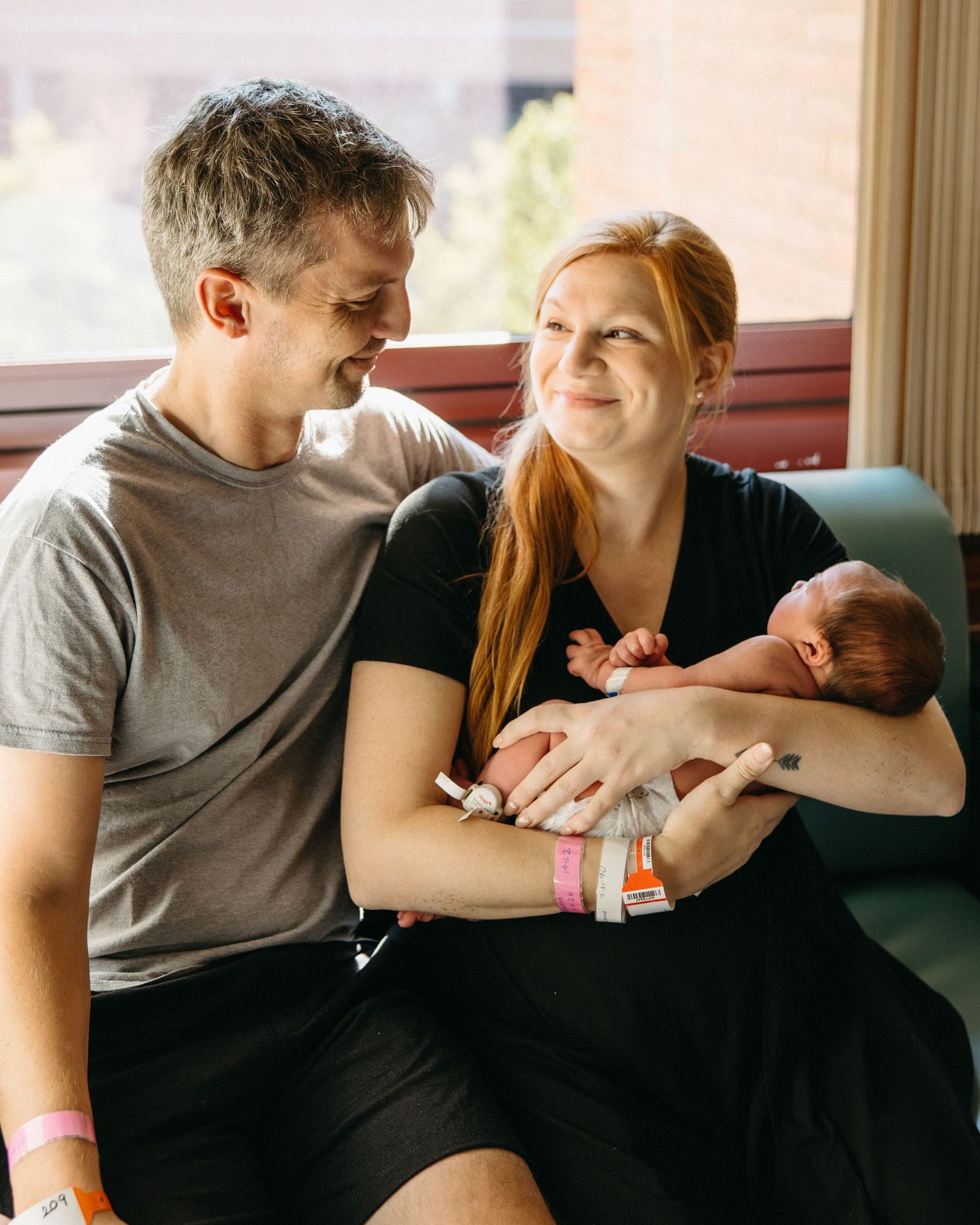 New parents smiling at each other while cradling their newborn baby in a hospital room.