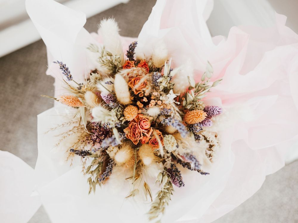 Rustic dried flower bouquet with orange roses, lavender, and pampas grass on white tissue paper.