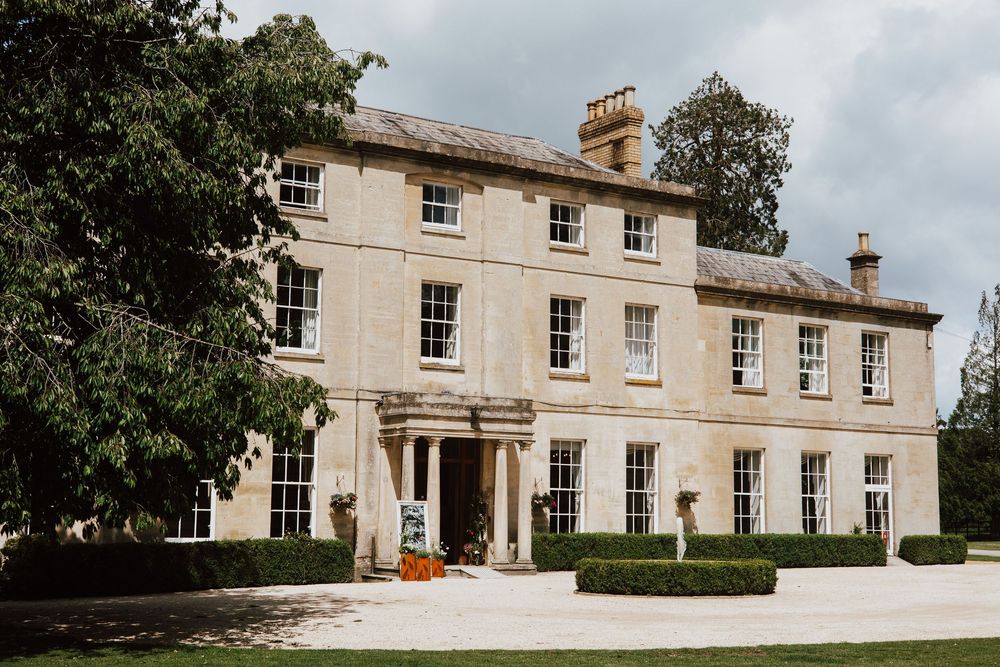 A grand Georgian country house with cream stone facade, sash windows, and manicured hedges set in lush green grounds.