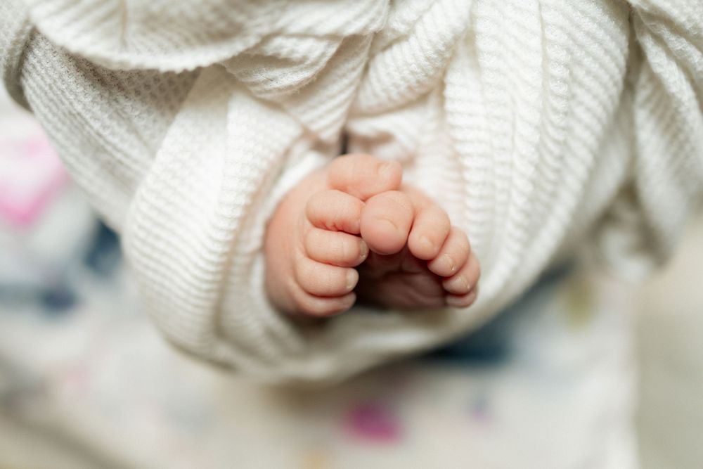 Close-up of a newborn baby's tiny hands gently clasped together, wrapped in a soft white knit blanket.