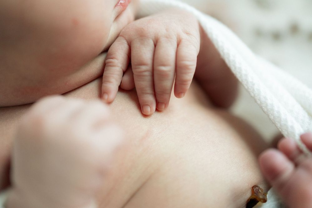 Close-up of a newborn baby breastfeeding, with tiny fingers resting on mother's chest.
