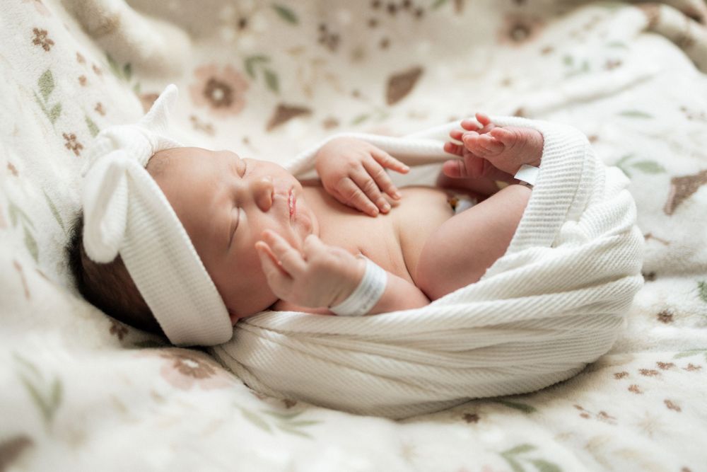 Newborn baby sleeping peacefully in a white knit bunny hat and blanket on a floral background.