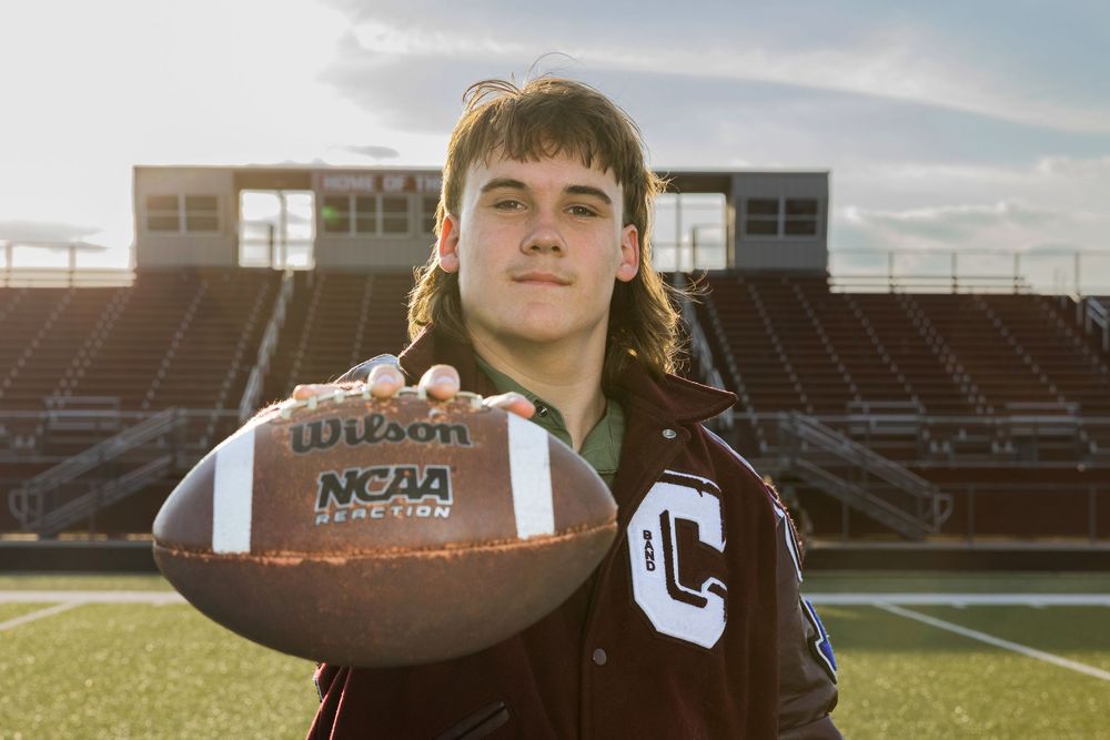 young man standing on a football field holding a football out in front of his face