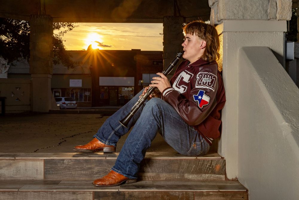young man perched on porch steps at sunset playing his clarinet, wearing his high school letterman jacket