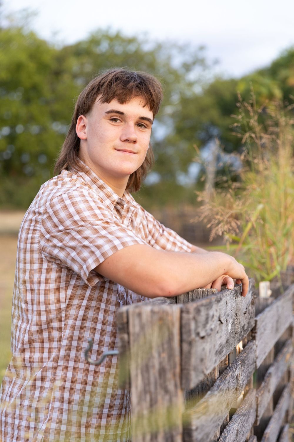 Young man standing next to wooden fence with arms resting on the fence