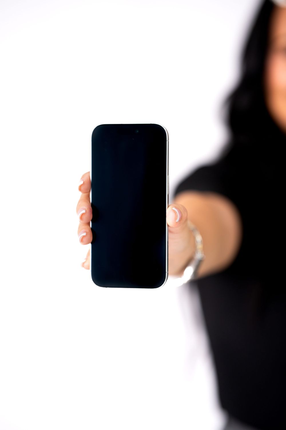 Person in black outfit holding smartphone with blank screen toward camera.