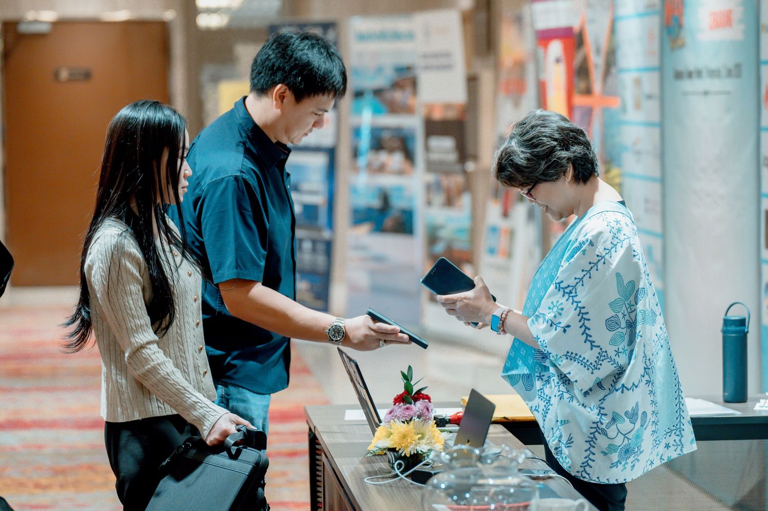 Two attendees check in with a registration staff member at a professional conference or business event.