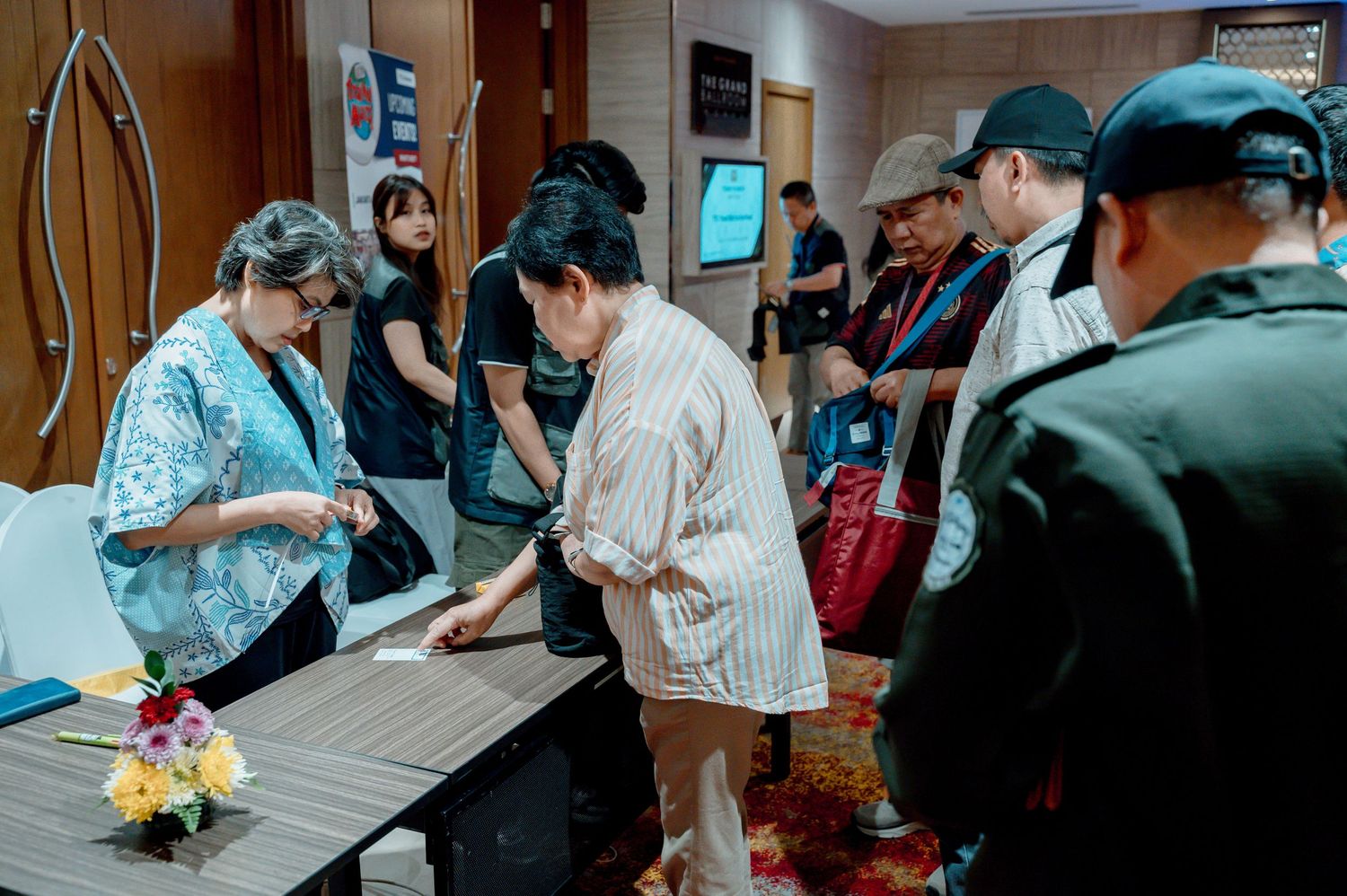 People checking in at a registration table in a conference hall, with security personnel standing nearby.