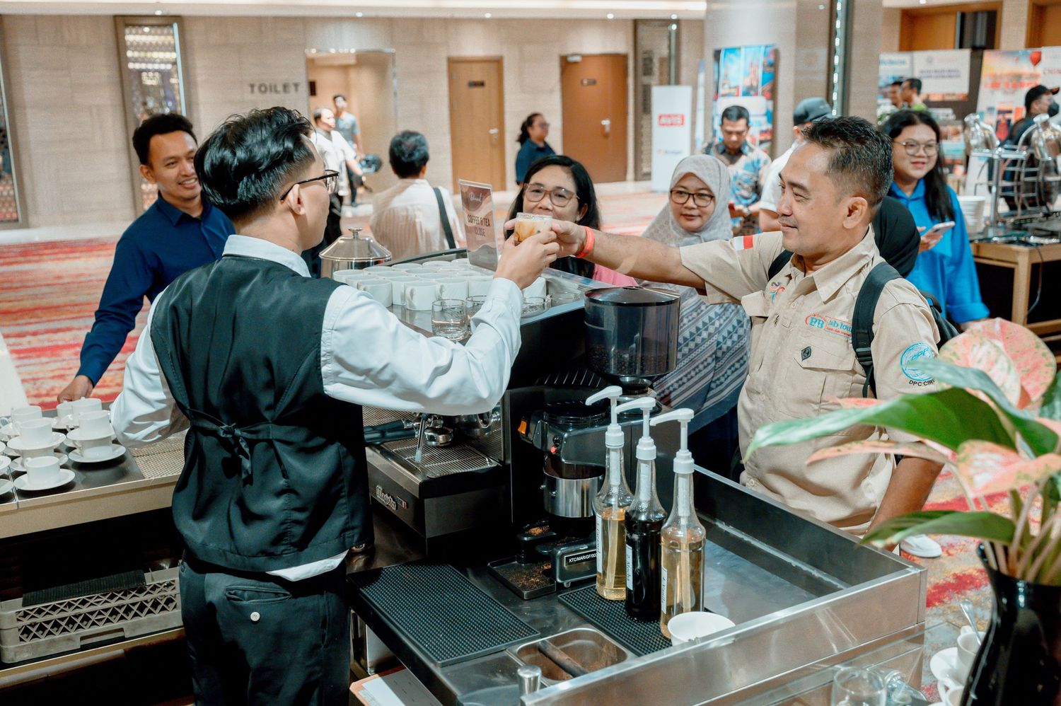 Barista serving coffee to guests at a busy hotel coffee station during a professional event.