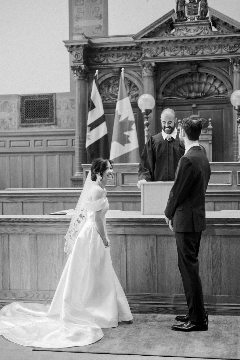 Bride and groom exchange vows before an officiant with Canadian flags in a classic ceremony hall.