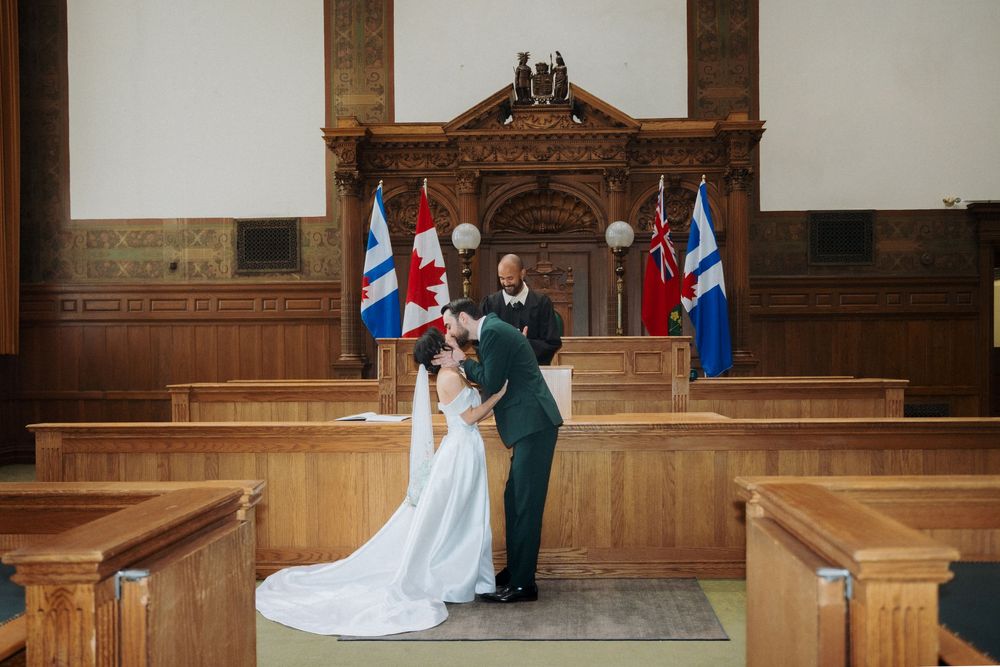 Bride and groom share a romantic moment in a wood-paneled courthouse ceremony hall with Canadian flags.