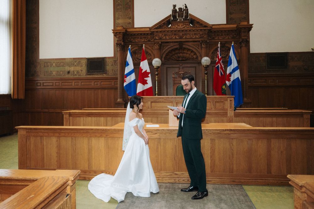 Bride and groom exchange vows in a elegant wood-paneled courthouse ceremony room with Canadian flags in the background.