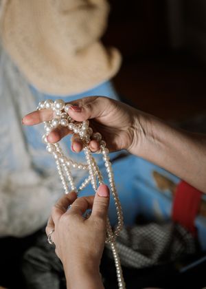 Hands holding multiple strands of white costume pearl necklaces.