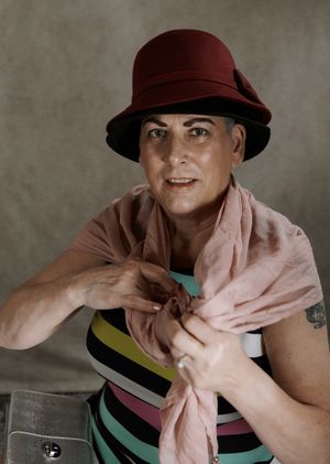 Woman wearing a red cloche hat and pink scarf over a striped top, posing confidently indoors.