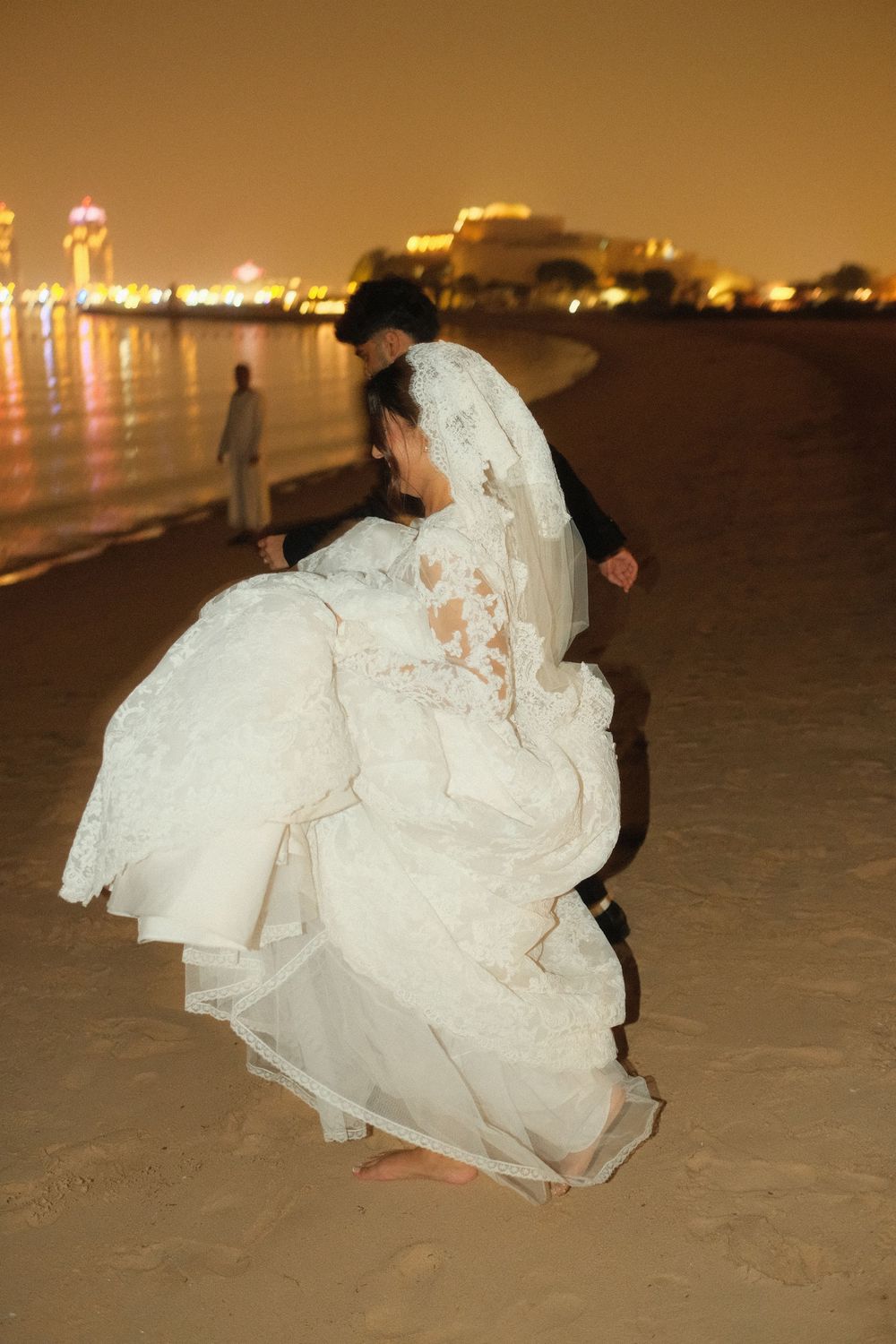 Bride in her white dress on the beach at night walking towards the sea in Doha, Qatar. The Chedi Katara hotel