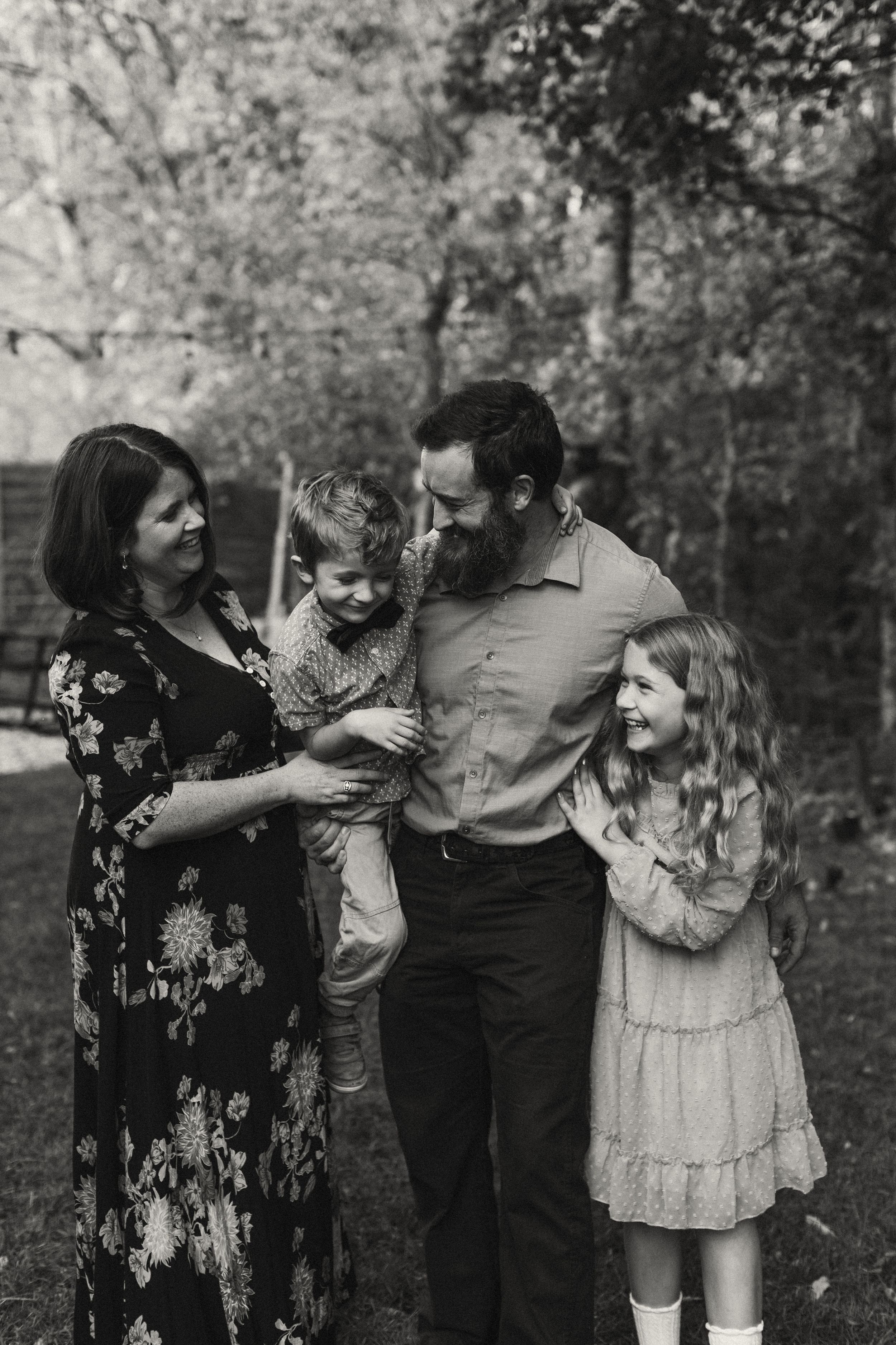A family shares a joyful moment together outdoors in black and white, dressed in casual attire against a natural background.