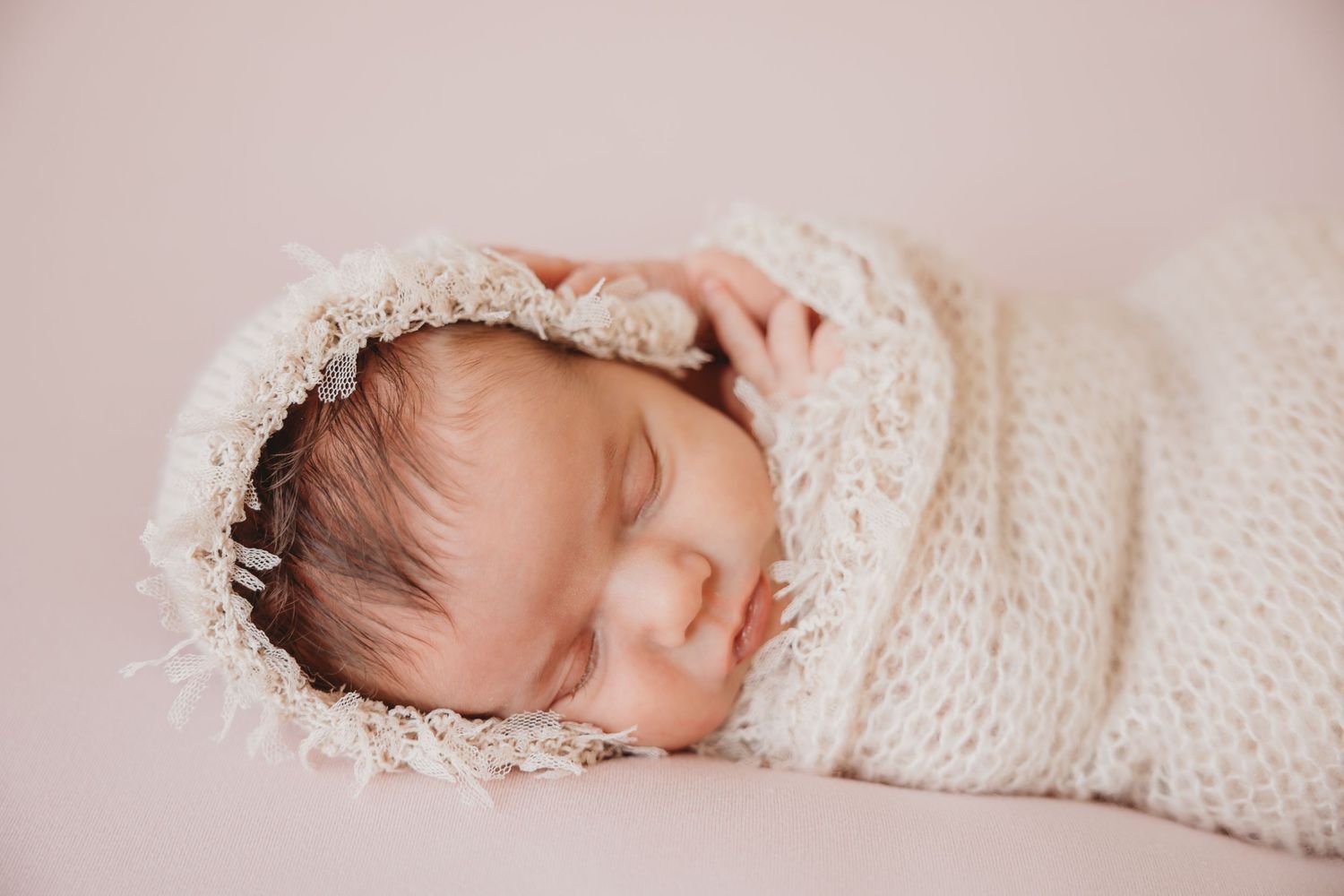 Newborn baby sleeping peacefully wrapped in cream colored knit blanket.